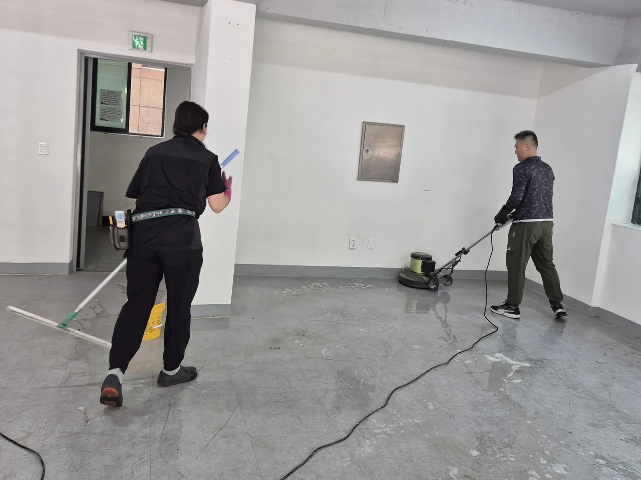 한쪽에서 폴리셔를 돌리고 다른 쪽에서 물기를 닦는 사무실 바닥 작업 현장