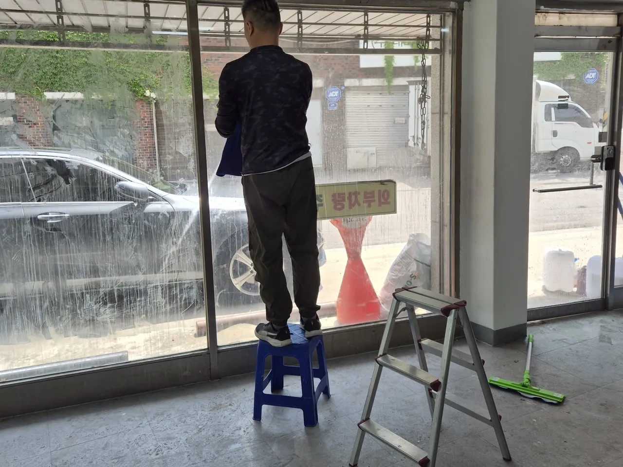 접이식 의자에 올라 통유리를 닦는 작업자